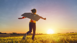 Child running through a field pretending to be a plane as the sun sets