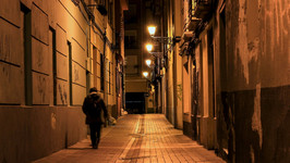 A lonely figure walks down a deserted city street at nighttime.