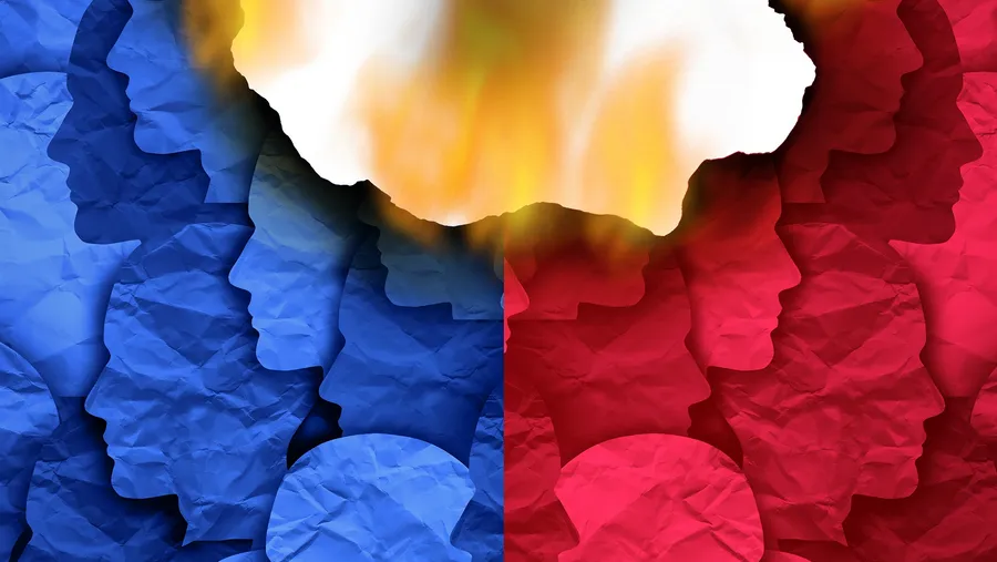 Illustration of two opposing human profiles made of layered blue and red paper cutouts facing each other, with a fiery burn hole in the center symbolizing intense political polarization or ideological conflict.