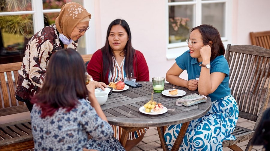An image of 4 diverse women in diverse clothing sitting outside of the Meierhof Building while enjoying their snacks.