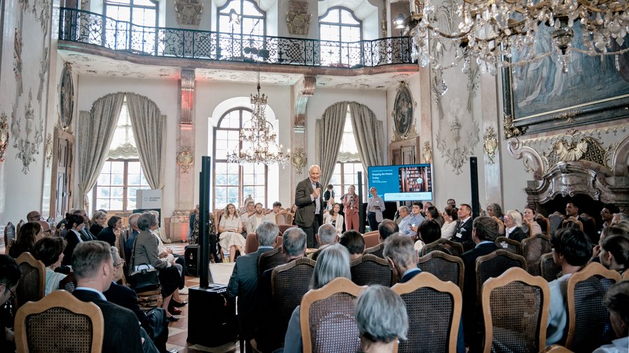 Martin Weiss, a man holding a microphone, stands in the middle of the Marble Hall and greets a seated audience.
