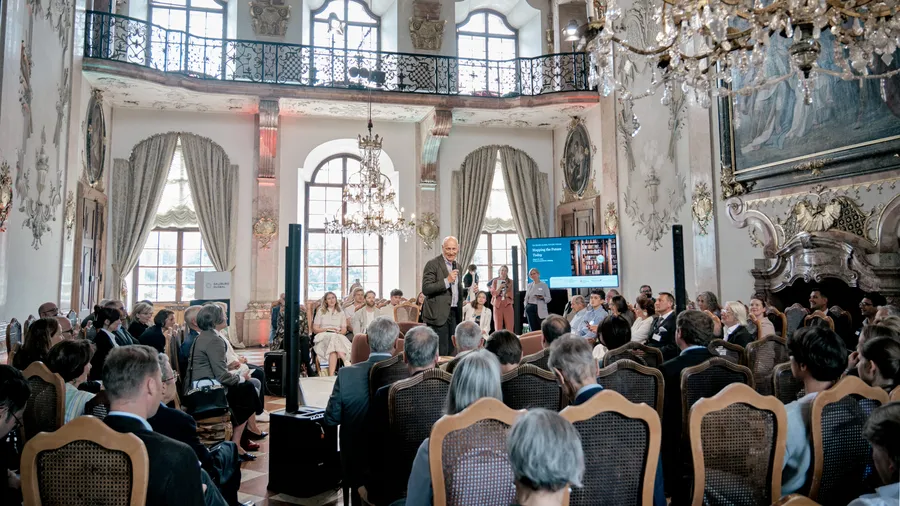 Martin Weiss, a man holding a microphone, stands in the middle of the Marble Hall and greets a seated audience.