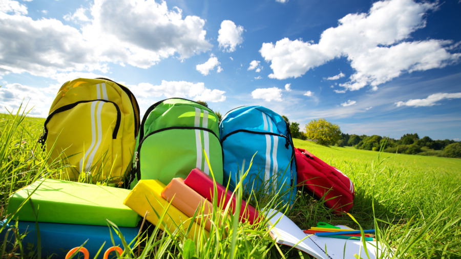 Colorful children schoolbags outdoors on a field of grass next to colorful books and notebooks