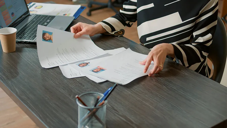 a woman's hands sort through a stack of CVs of potential job candidates