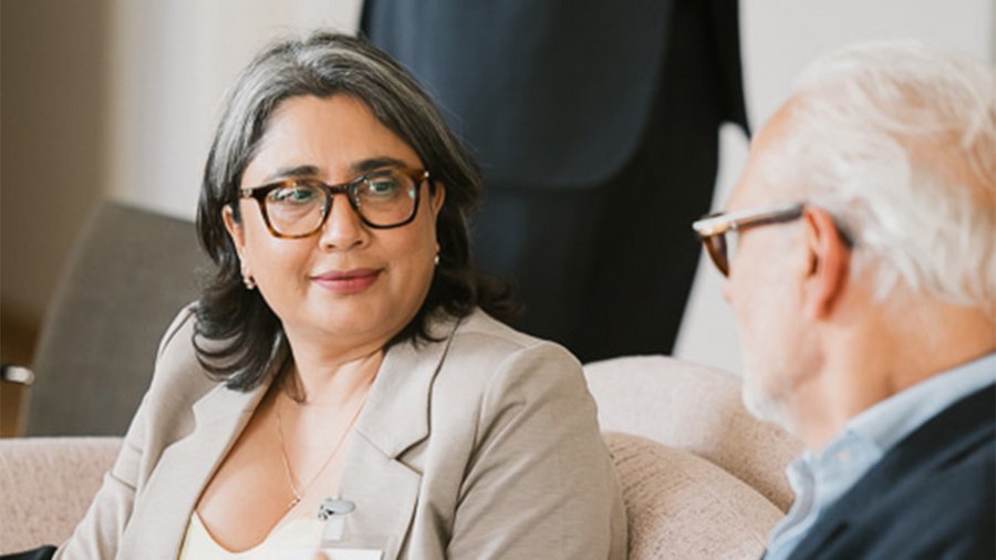 a woman with dark hair and glasses sits looking to the right