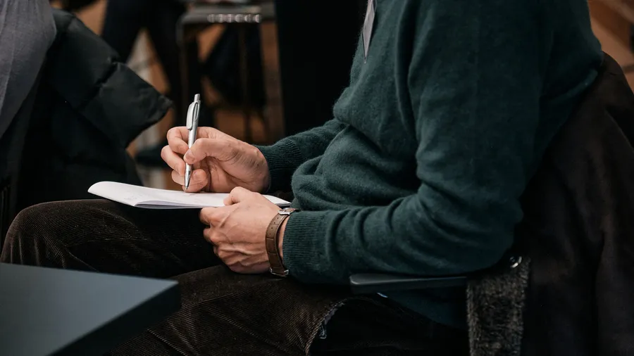 A man in a sweater writes notes in a notebook.