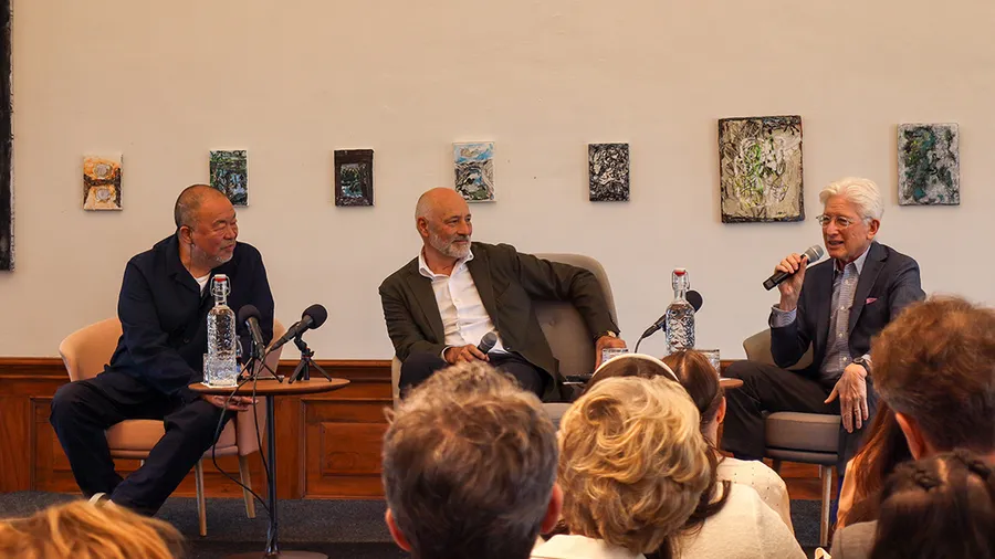 three men sit on a stage talking together in front of an audience
