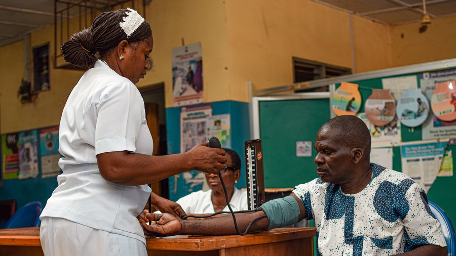 A female nurse measures the blood pressure of a male patient who is seated.