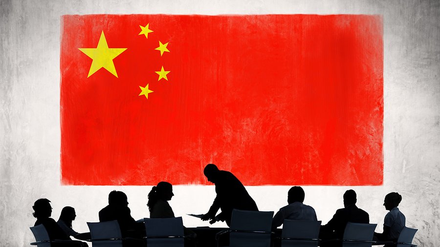 a group of figures sitting around a business table, with a chinese flag in the background
