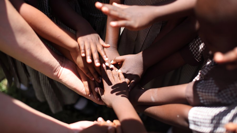 A group of children placing their hands together in a circle, symbolizing unity and teamwork.