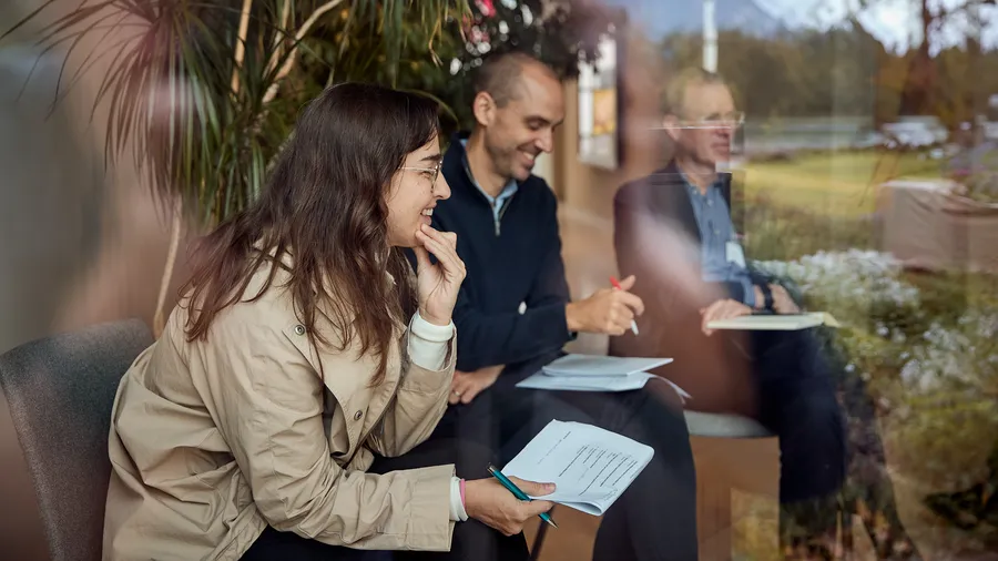 A woman sits in the foreground smiling while taking notes, with two others behind her.