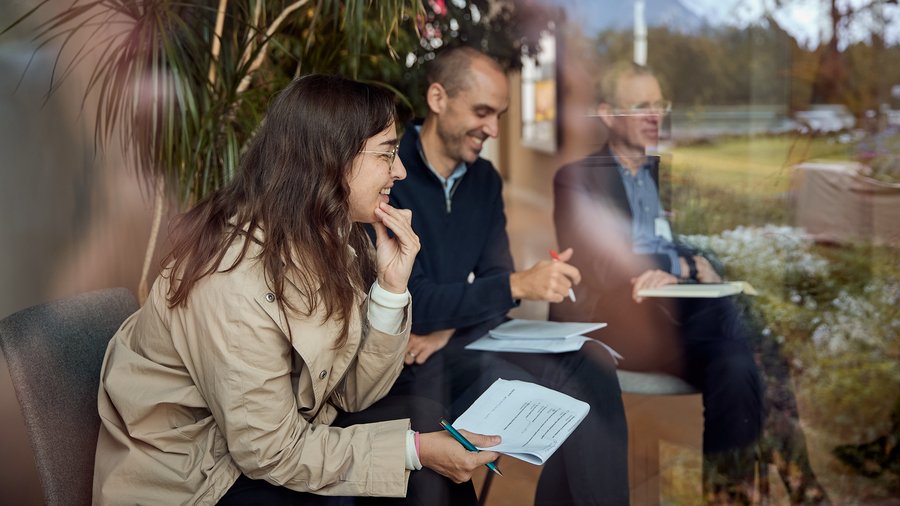A woman sits in the foreground smiling while taking notes, with two others behind her.