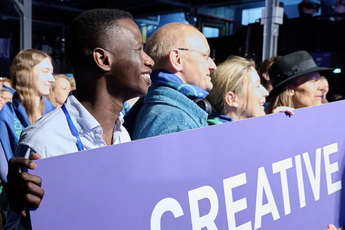 a man is smiling alongside several other people as they hold a sign that reads "creative"