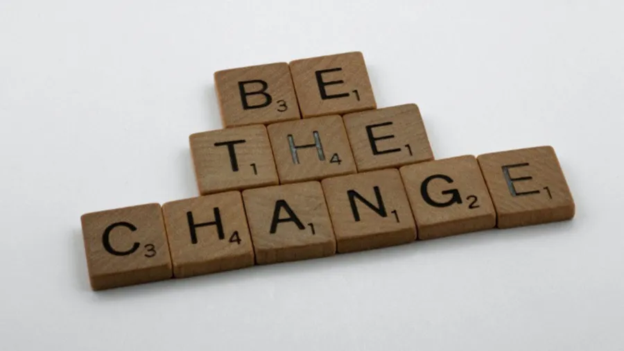 A few blocks of letters are carefully arranged on a flat surface to spell out 'be the change'