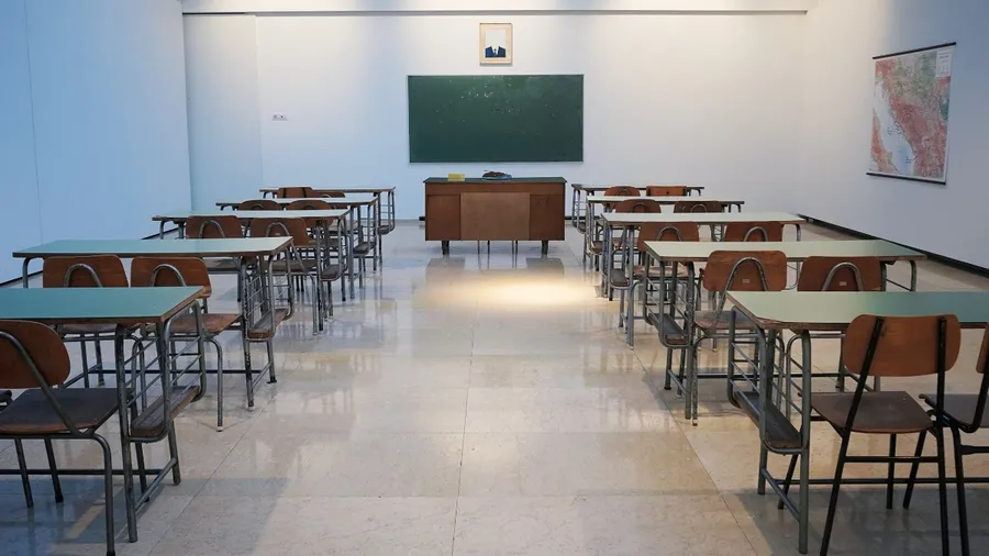 An empty classroom full of desks and chairs, with a chalkboard in the front. 