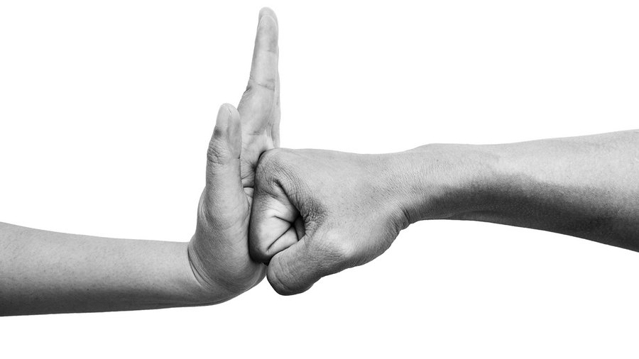 A black and white photo of a person's palm stopping another person's fist. 
