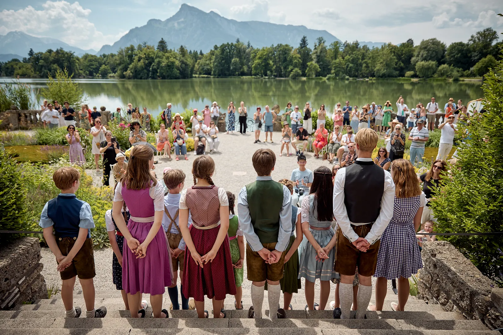 a group of young people dressed in Austrian traditional clothing performing in front of a crowd on the terrace of Schloss Leopoldskron