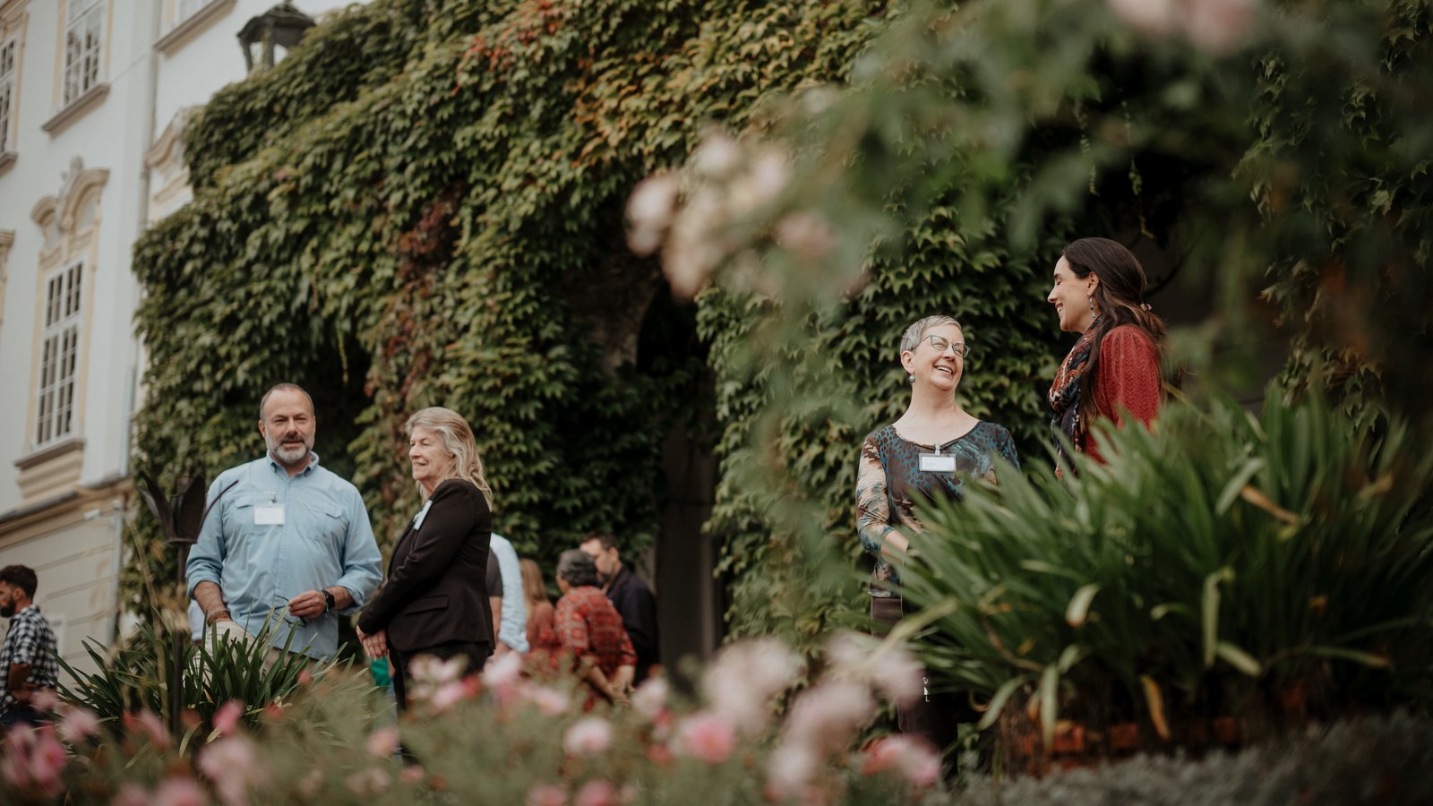 individuals stand outside talking with lots of greenery in the background