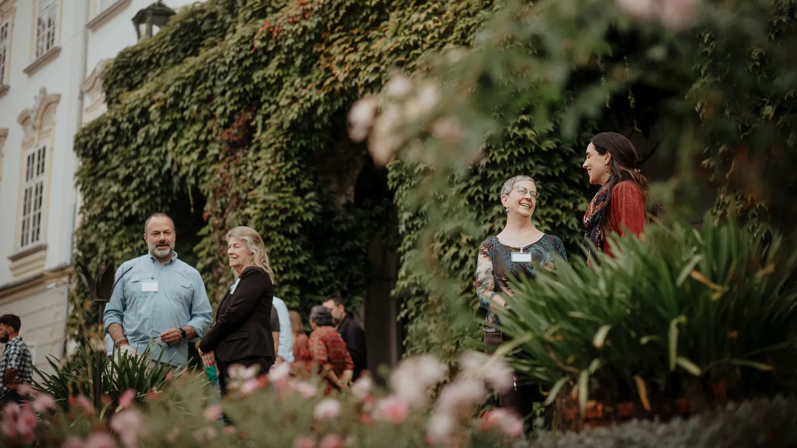 individuals stand outside talking with lots of greenery in the background
