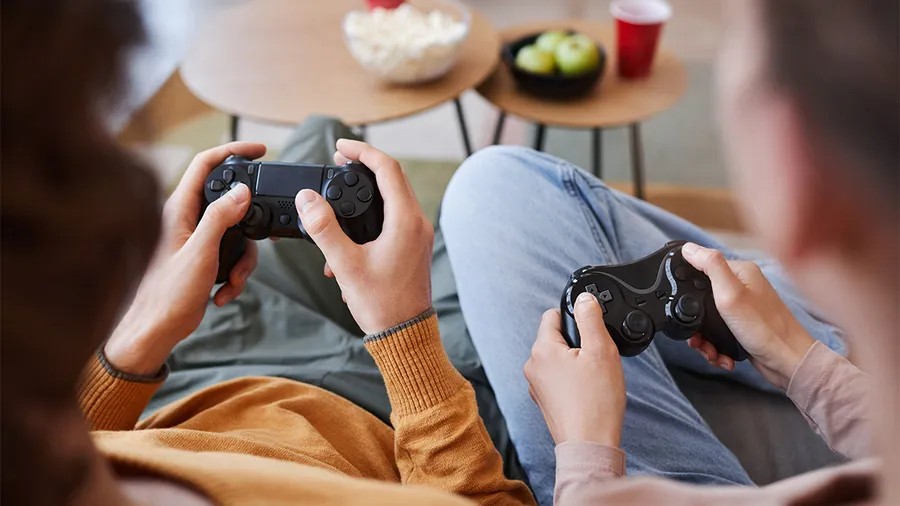 Two people sit on the couch playing a video game and we see their hands holding remote controls.