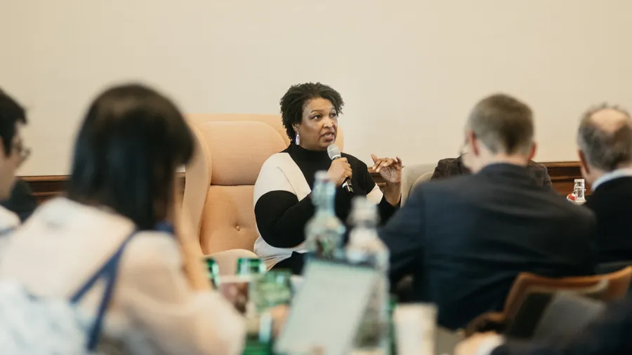 a woman speaks into a microphone in front of a seated crowd