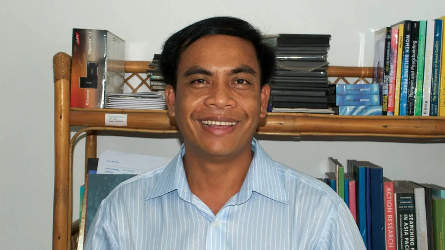 Photo of Khet Long in front of a bookshelf.