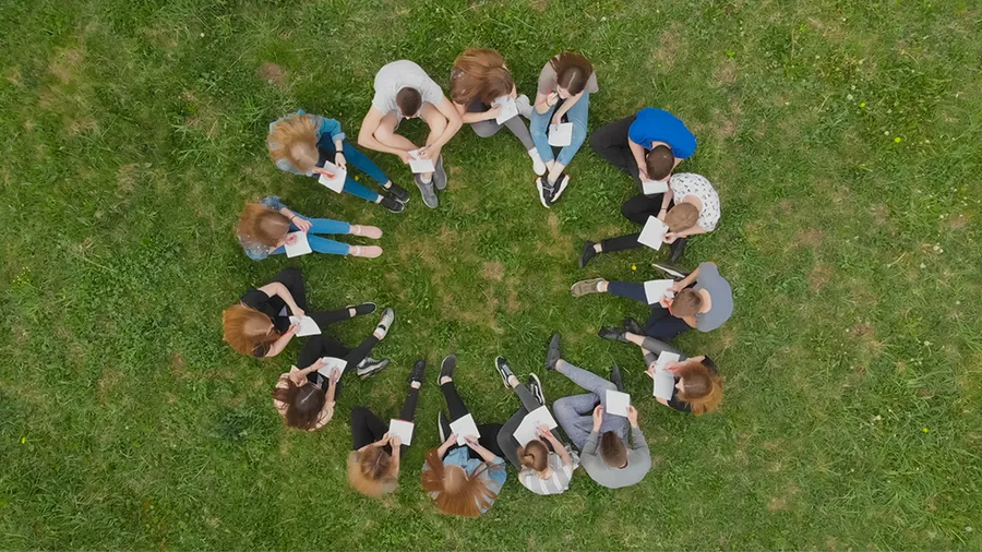 a group of students sit in a circle outside on grass