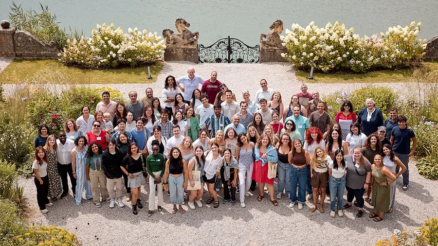 a group of around 90 people stand outside smiling up at the camera