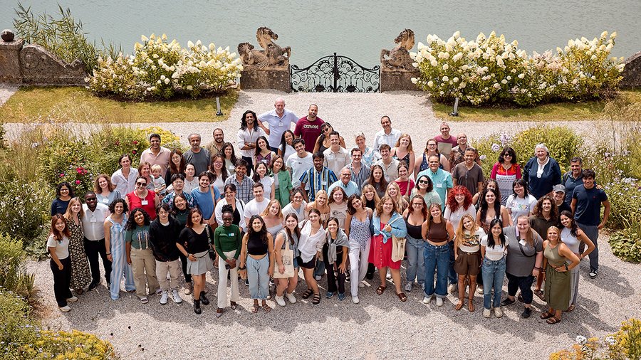 a group of around 90 people stand outside smiling up at the camera