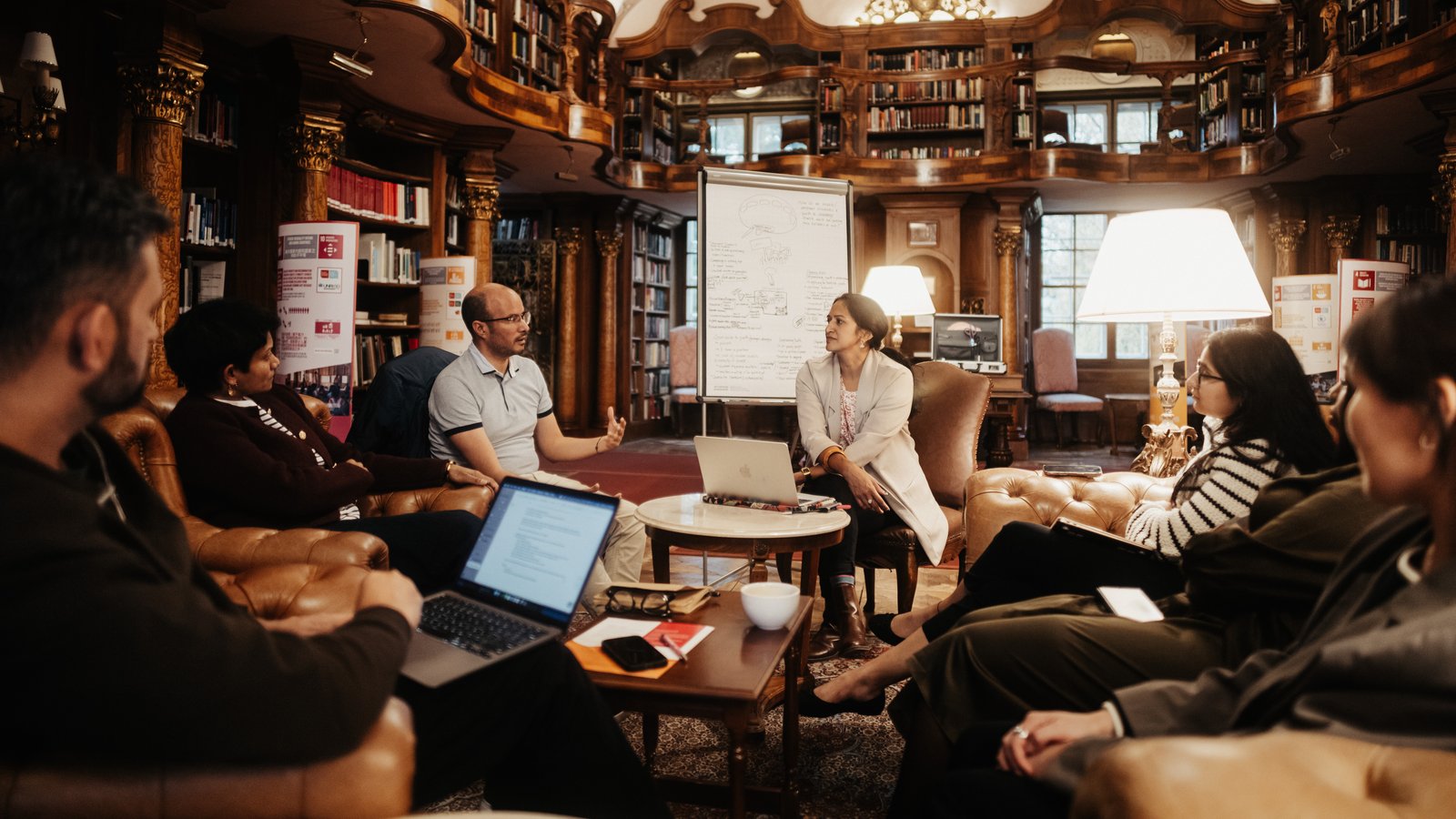 a group of individuals sit in a circle in the Max Reinhardt Library while having a discussion