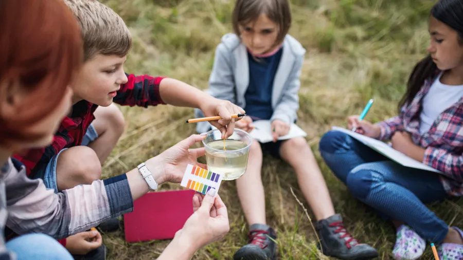 Group of school children with teacher on field trip in nature, learning science.