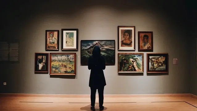 A woman stands in front of an art exhibition of painting and portraits in a museum.