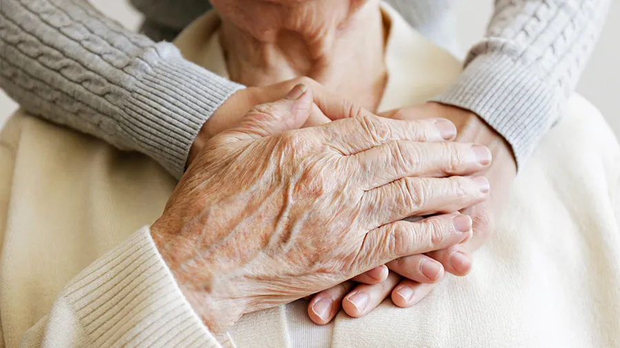 an elderly woman holds the hands of her caregiver on her chest