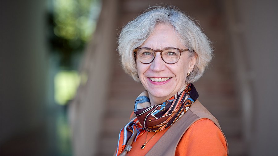 A woman with short hair and glasses smiles into the camera