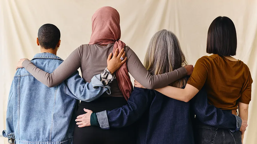 a group of several women stand facing away from us with their arms wrapped around each others shoulders