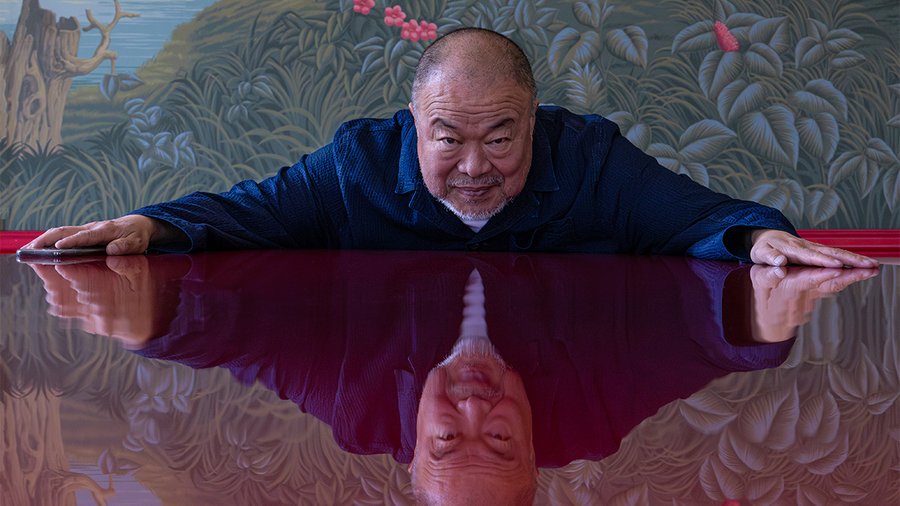 a man wearing a blue shirt leans forward on a reflective table