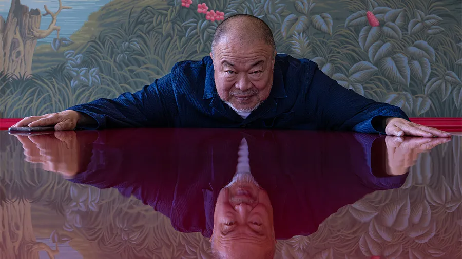 a man wearing a blue shirt leans forward on a reflective table