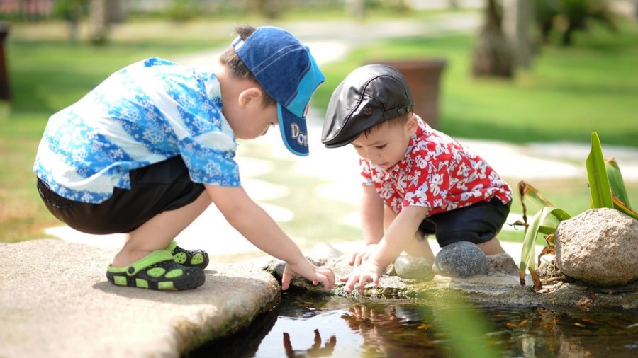 Two young children play together at the edge of a pond