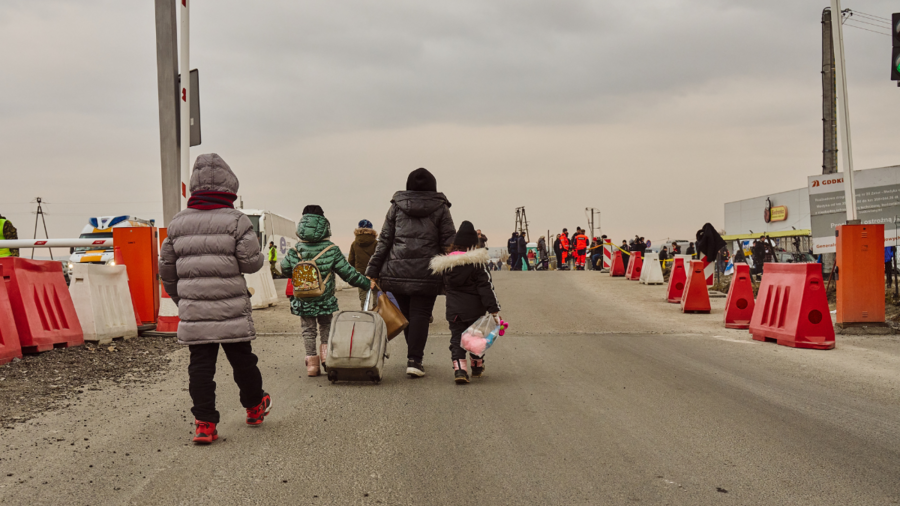 Three children and an adult with bags and a suitcase walking away