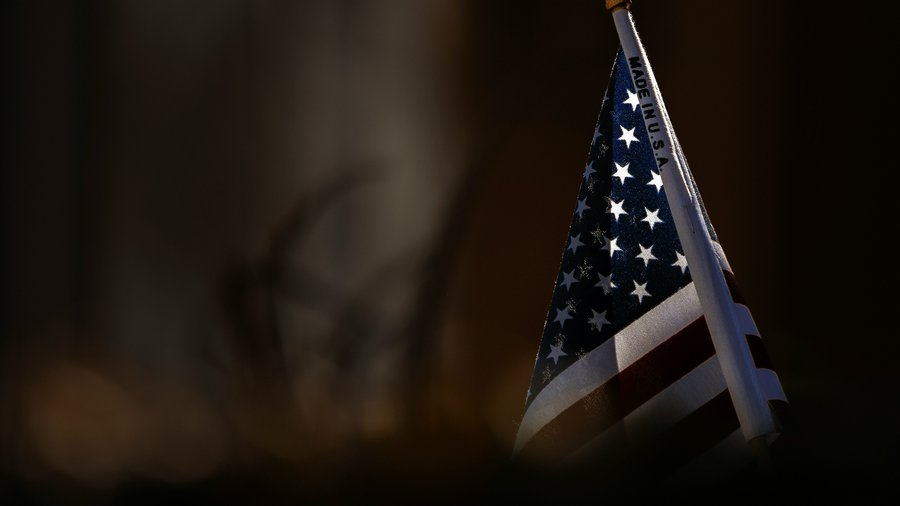 An american flag emerges from the shadows with the words "Made in U.S.A." written on the flagpole