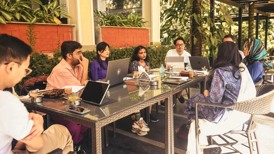 A group of people sitting outside in Bangalore working together on laptops while discussing.
