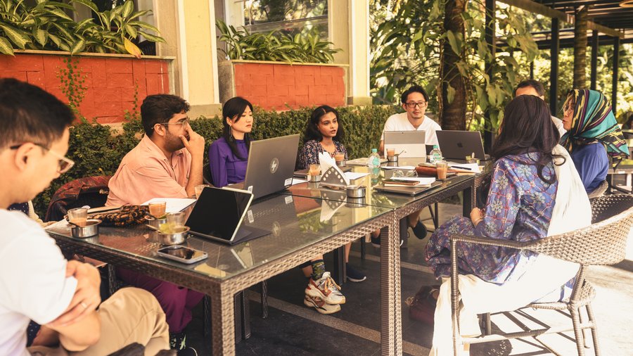 A group of people sitting outside in Bangalore working together on laptops while discussing.