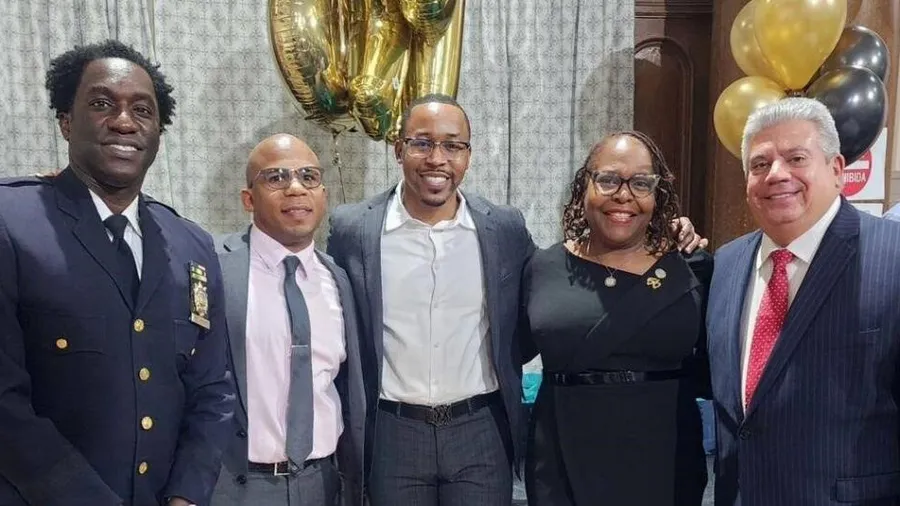 Community leaders and law enforcement officials pose together at a public safety and justice reform event, featuring gold and black celebration balloons.