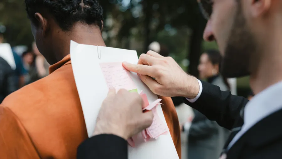 a man attaches a paper with writing on it to another man's back in a teamwork exercise