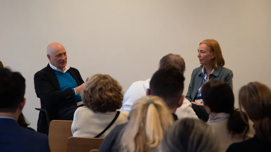a man sits on the left and speaks to woman with red hair in front of an audience