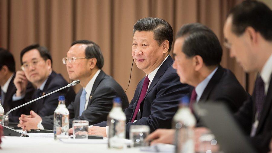 the president of china, xi jinping, sits at a negotiating table next to his colleagues