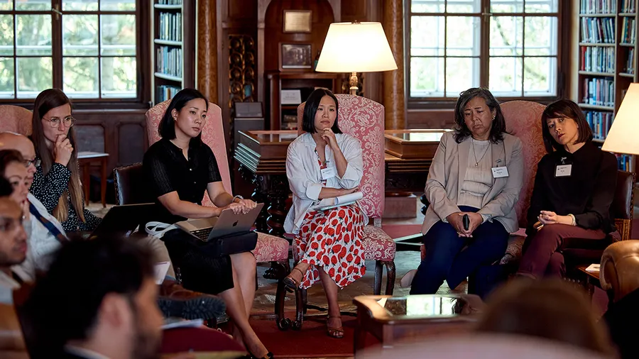 A diverse group of individuals, mostly women, sitting in a circle in the Max Reinhardt Library, attentively engaged in a discussion.
