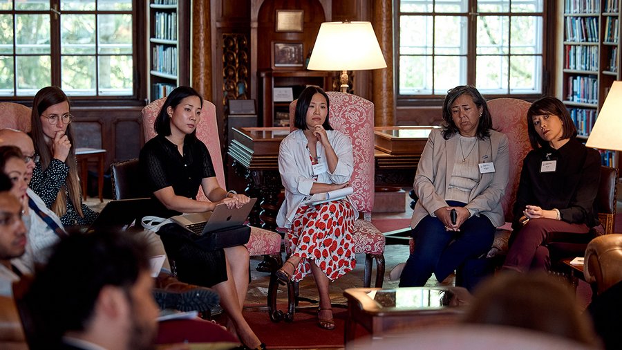 A diverse group of individuals, mostly women, sitting in a circle in the Max Reinhardt Library, attentively engaged in a discussion.
