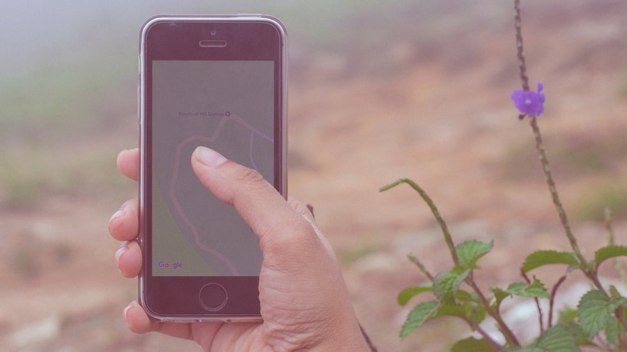 Person holding iPhone, looking at Ponmudi Hill Station on Google Maps