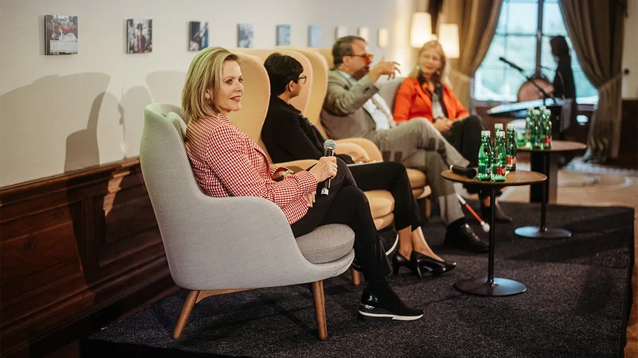 Renée Fleming sits in a gray chair next to three other individuals during a panel discussion